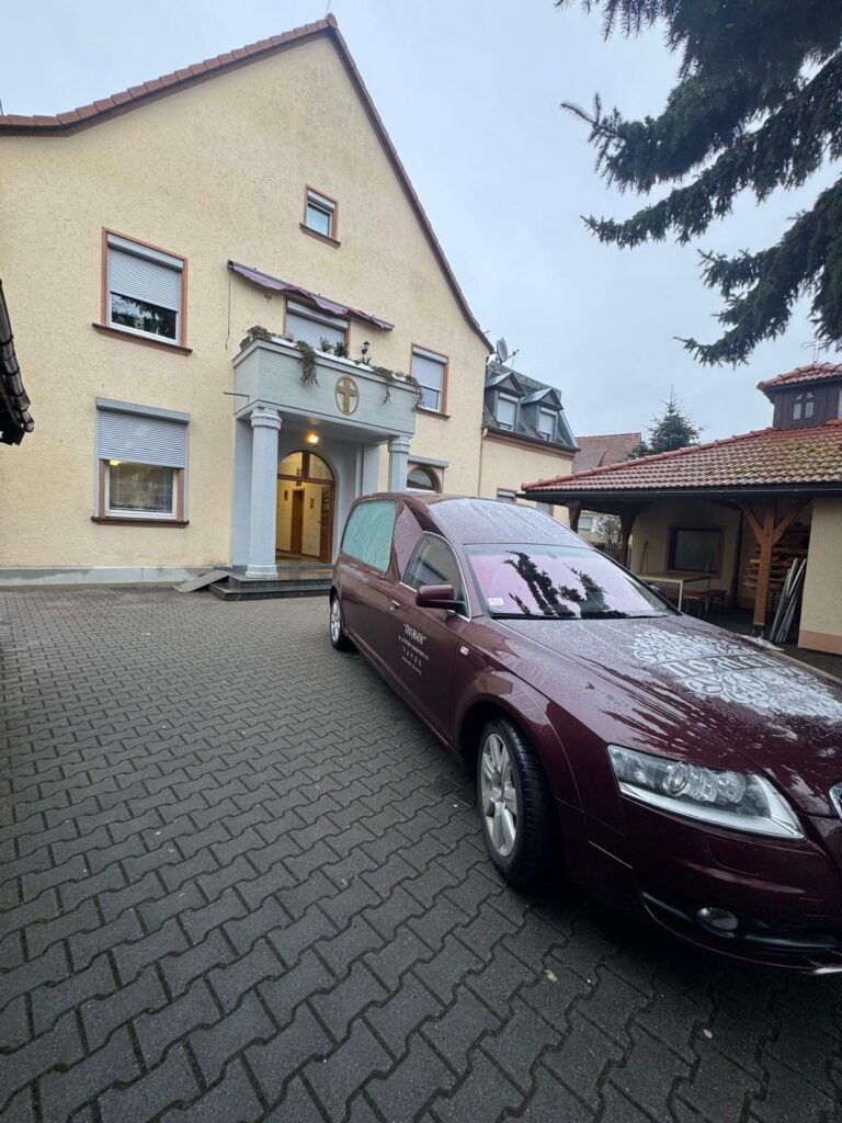 Vozilo Pogrebne opreme Pomen u dvorištu objekta sa krstom iznad ulaza, u inostranstvu