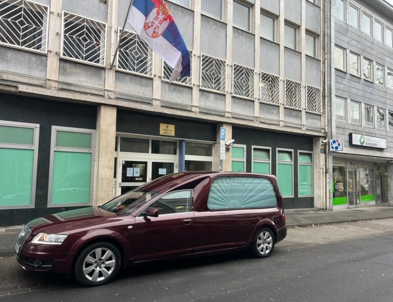 Vozilo Pogrebne opreme Pomen ispred zgrade sa zastavom Srbije, u inostranstvu